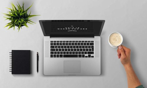 Persoon die gefrustreerd naar een laptop kijkt met een notitieboek op het bureau