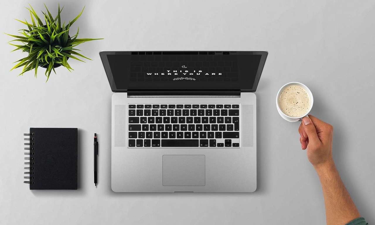 Persoon die gefrustreerd naar een laptop kijkt met een notitieboek op het bureau