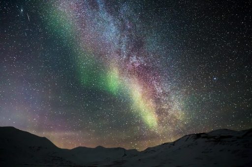 Groen noorderlicht zichtbaar aan een donkere sterrenhemel boven een open landschap
