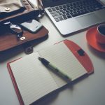 Een notitieboek, pen en laptop naast elkaar op een bureau, als symbool voor verschillende planningssystemen