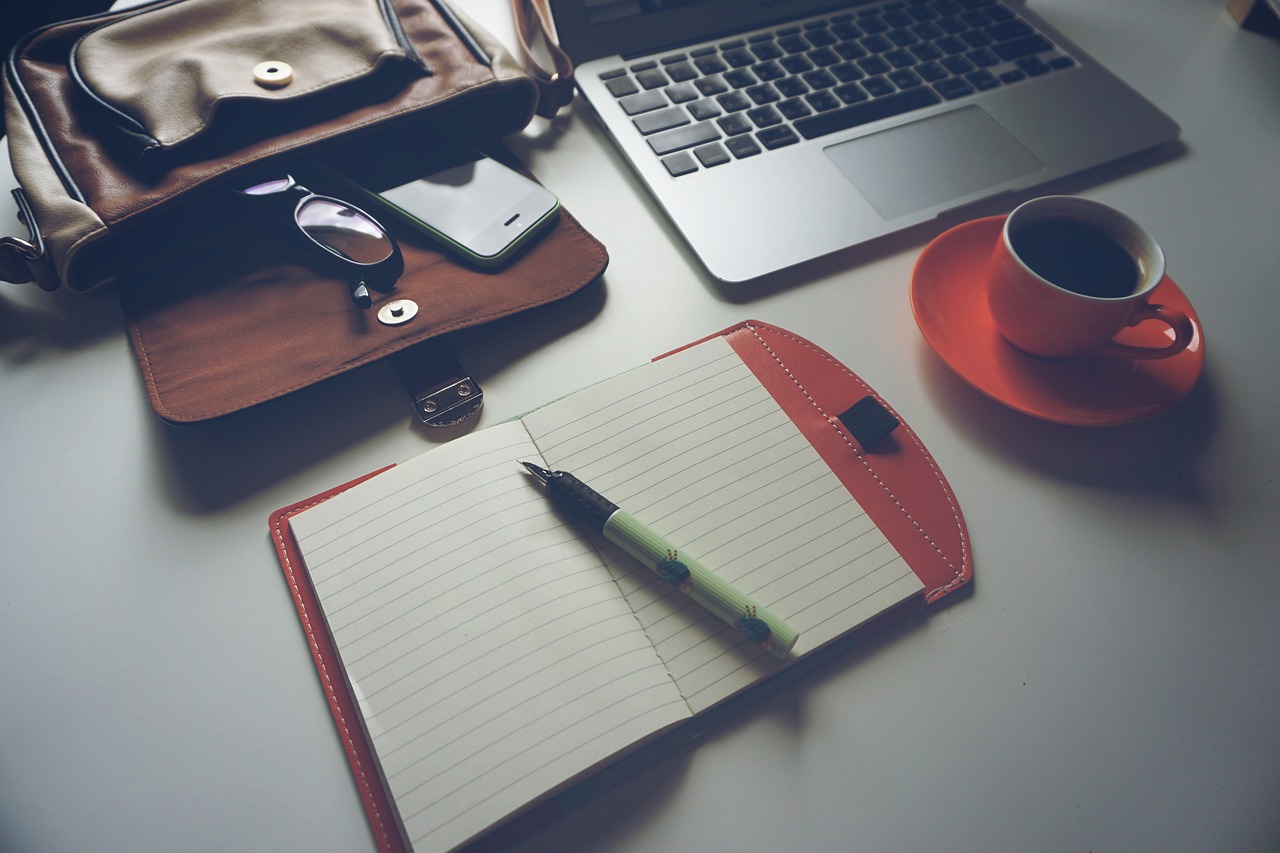 Een notitieboek, pen en laptop naast elkaar op een bureau, als symbool voor verschillende planningssystemen